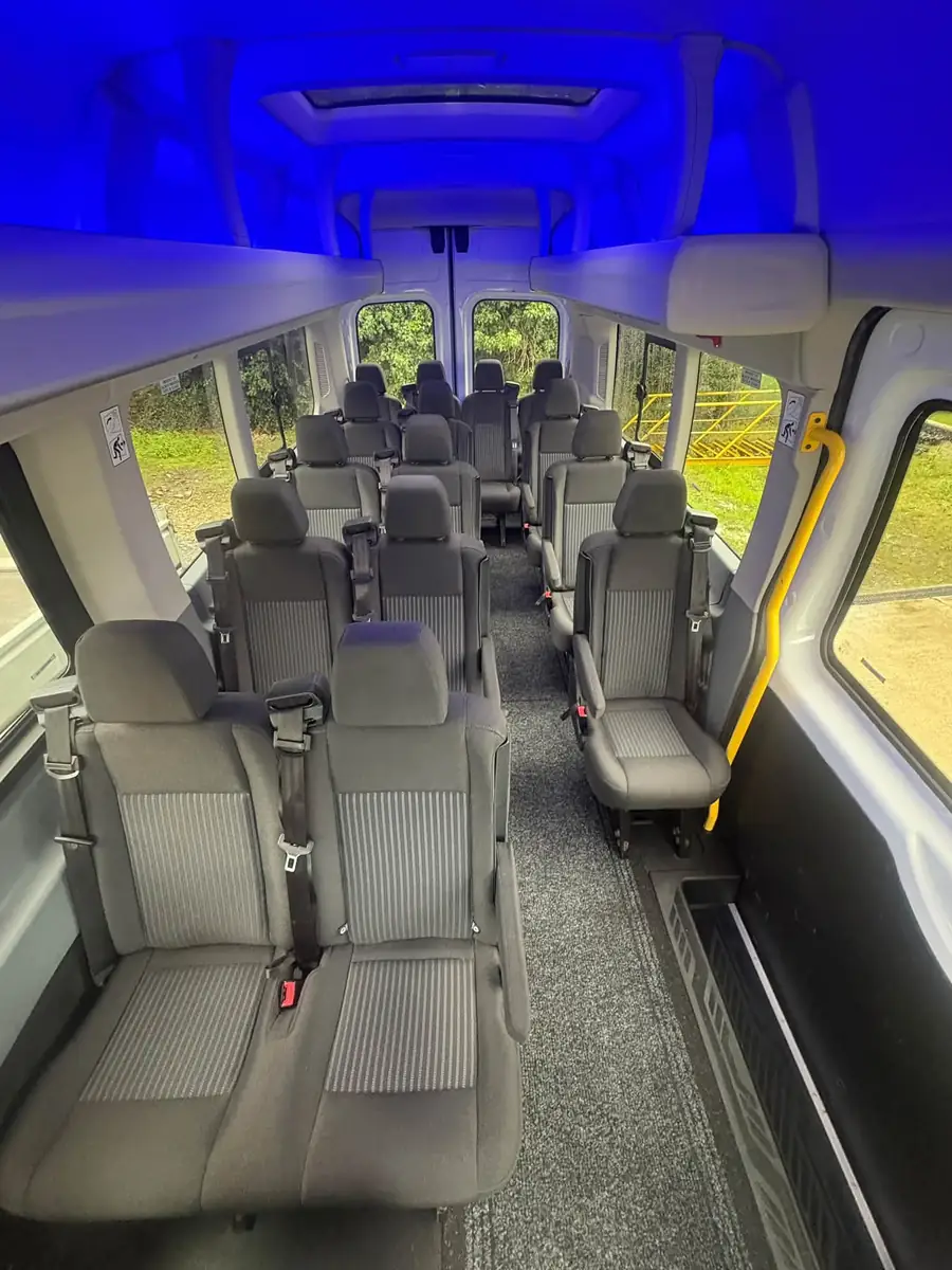 View down the aisle of the minibus: grey reclining seats with seatbelts and blue ceiling light