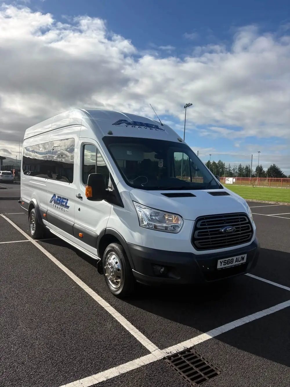 The white Abel Travel Ford Transit minibus with its blue logo, parked in the sun